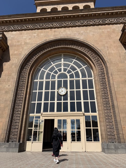 A traveler walking toward the grand arched clock entrance of a railway station, Yerevan Railway Station, Armenia