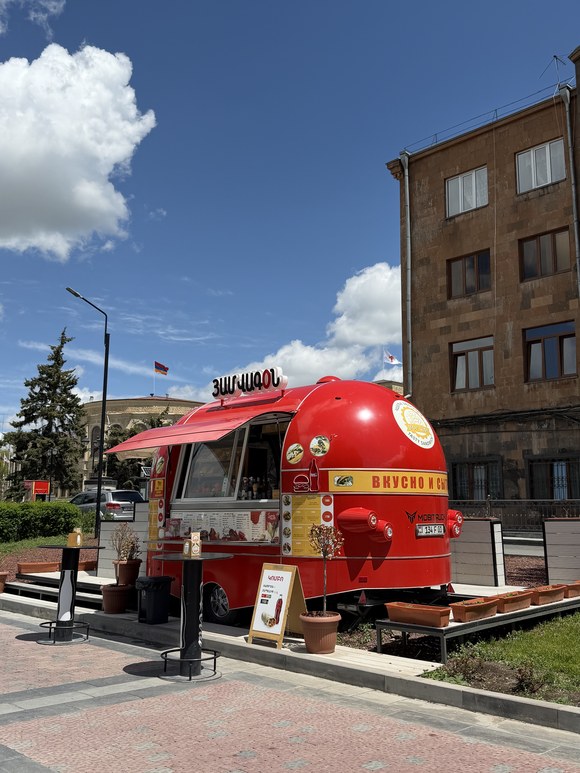 A red food truck parked on a paved plaza with a stone building behind, St. All Saviors Church, Armenia