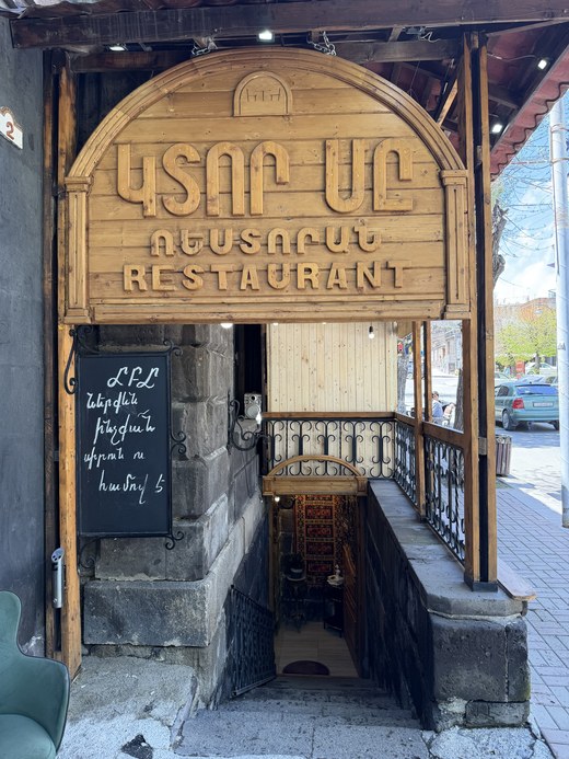 A carved wooden sign over stairs descending to a basement restaurant, Gyumri, Armenia