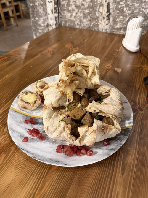 A lavash-wrapped meat dish plated with roasted mushrooms and pomegranate seeds, Gyumri, Armenia