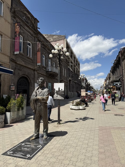 A bronze statue on a pedestrian street lined with historic buildings and lampposts, Gyumri, Armenia