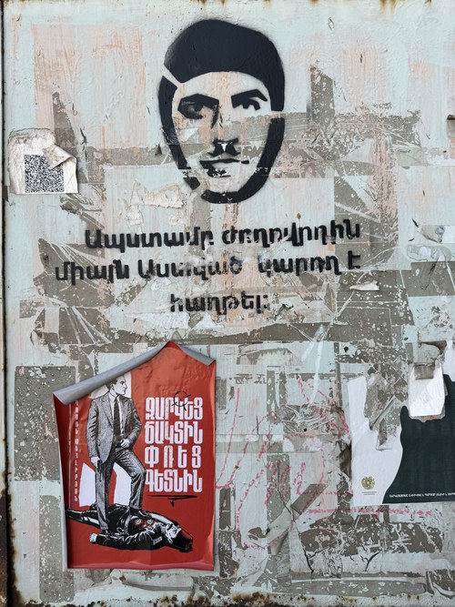 Weathered wall with stencil art and layered political posters in Armenian, Gyumri, Armenia
