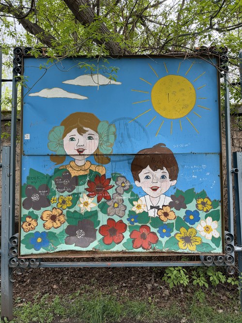 A weathered mural of two children among flowers under a painted sun, Central Park, Armenia