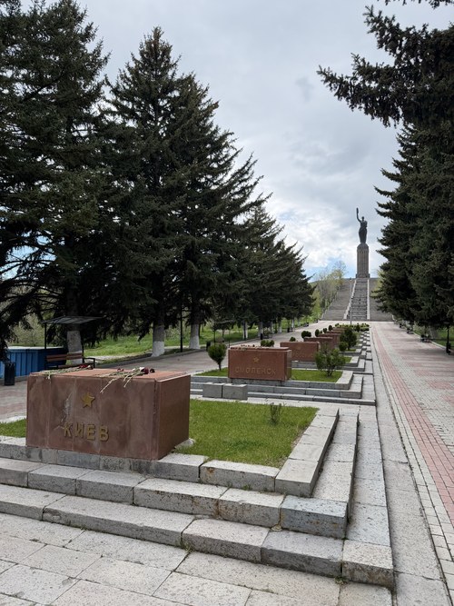 Memorial stone blocks lining a pine-lined path leading up to the distant Mother Armenia statue, Gyumri, Armenia