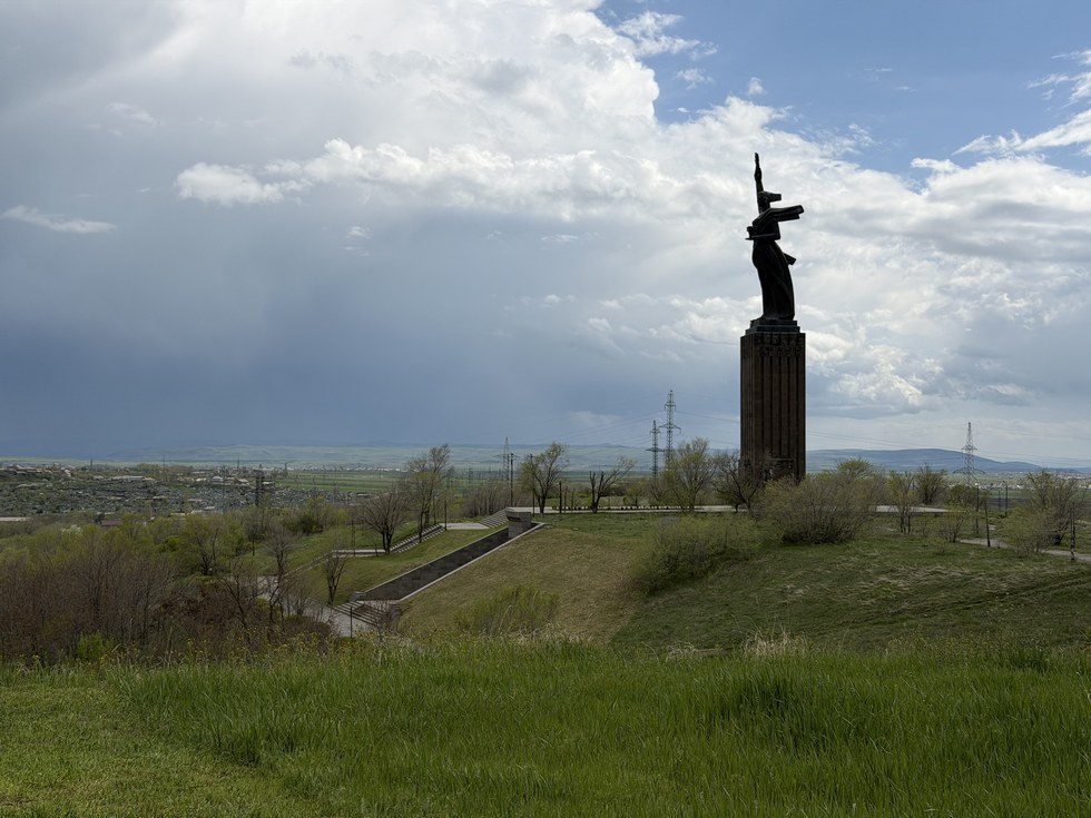 A statue atop a tall stone tower overlooking green hills and a distant valley, Black Circular Fortress, Armenia