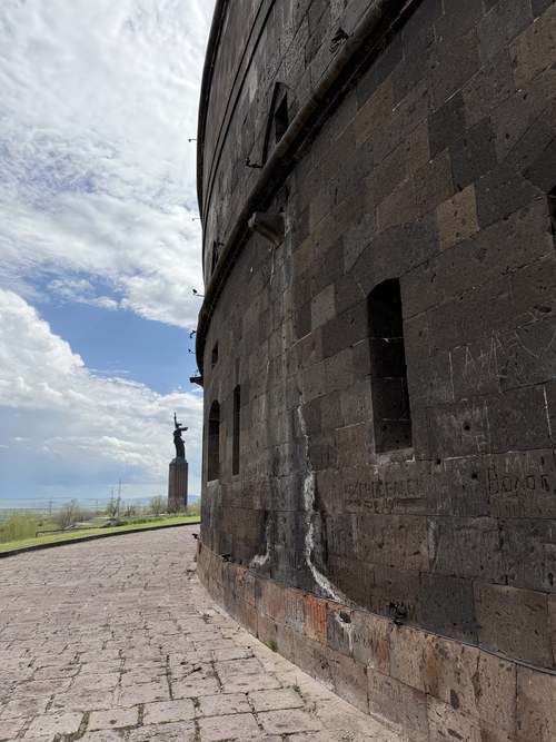 A path along the dark stone walls of the Black Fortress with the Mother Armenia statue in the distance, Gyumri, Armenia