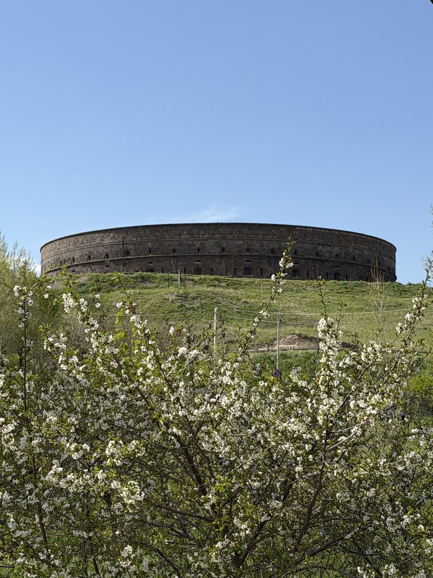 The circular walls of a hilltop fortress rising behind blossoming trees, the Black Fortress, Gyumri, Armenia
