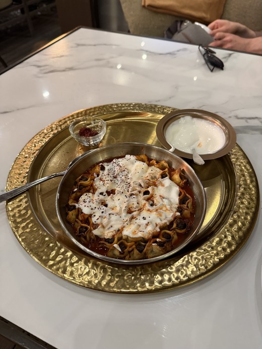 A bowl of manti dumplings topped with yogurt and chili oil served on a gold tray, Mayrig Yerevan, Armenia