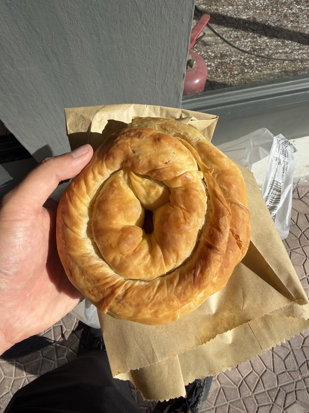 Hand holding a coiled golden phyllo pie on a paper bag, Thalia Rooms, Greece