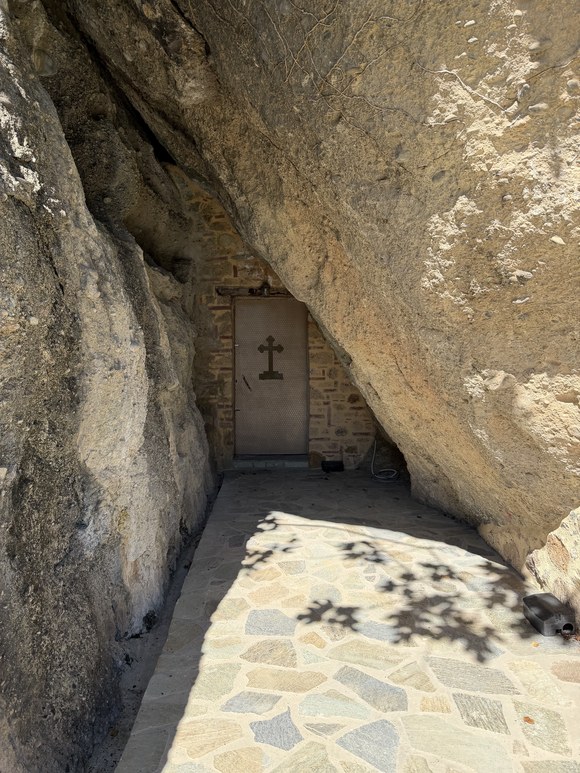 Stone-paved alcove under an overhanging rock leading to a small door marked with a cross, Meteora, Greece