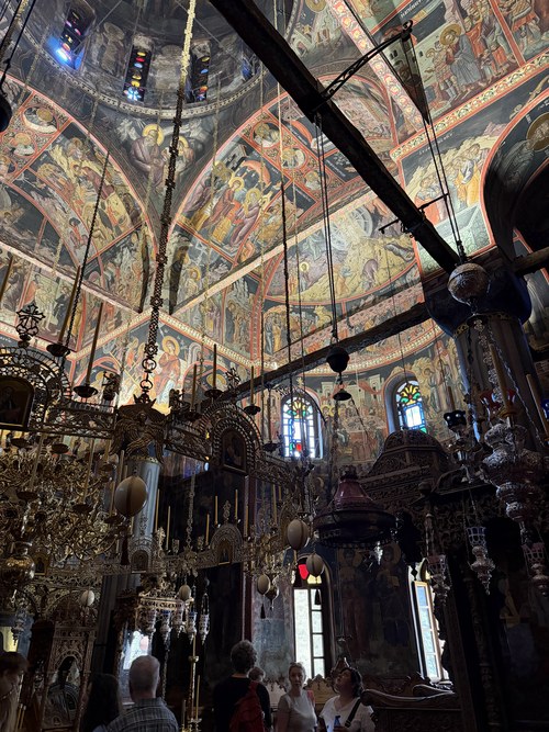 Visitors beneath a fresco-covered dome and hanging brass chandeliers inside a church, Great Meteoron, Greece