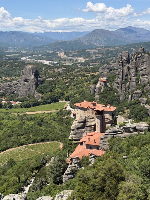 Red-roofed monastery on a rocky ledge above vineyards, valley and mountains, Viewpoint Meteora, Greece