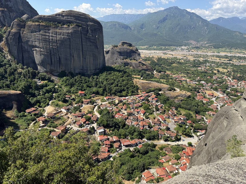 Red-roofed village below huge rock towers and green mountains, seen from a rocky overlook, Meteora, Greece