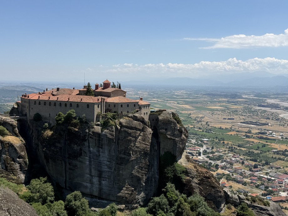 Red-roofed monastery on a sheer rock cliff above a wide farm valley and town, St. Stephen (Agios Stefanos), Greece