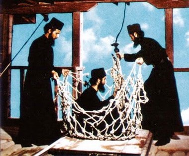 Monks in black robes holding open the rope net once used to haul people and supplies up to the monasteries, Meteora, Greece