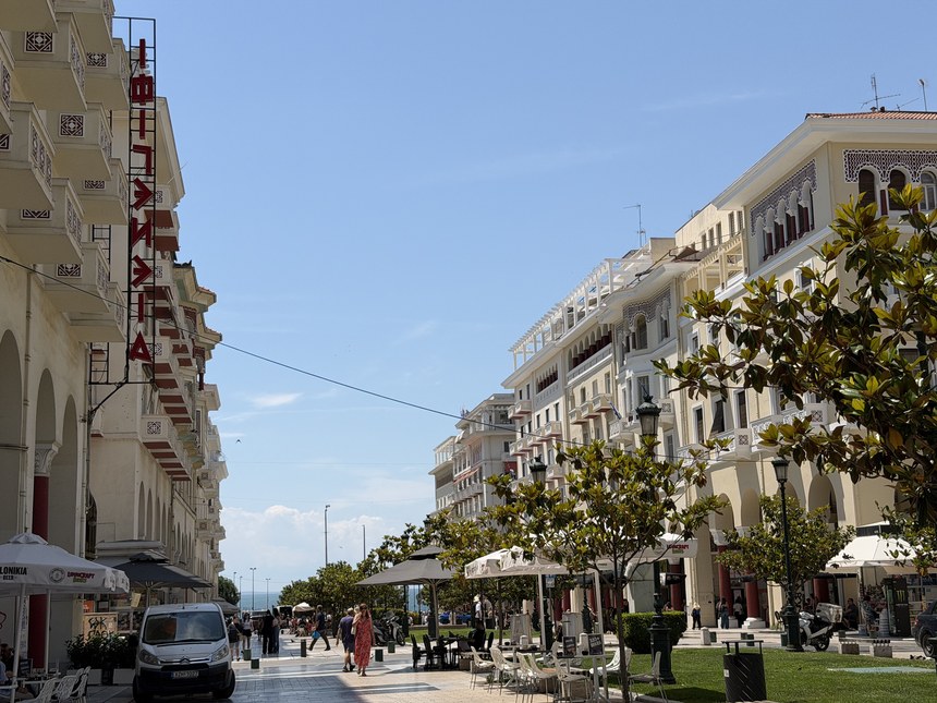 A wide pedestrian boulevard lined with ornate buildings and outdoor cafe tables, Kapani Market, Greece