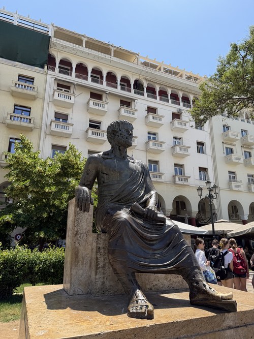 A bronze seated statue of a robed figure in front of an arcaded building, Platia Aristotelous, Greece