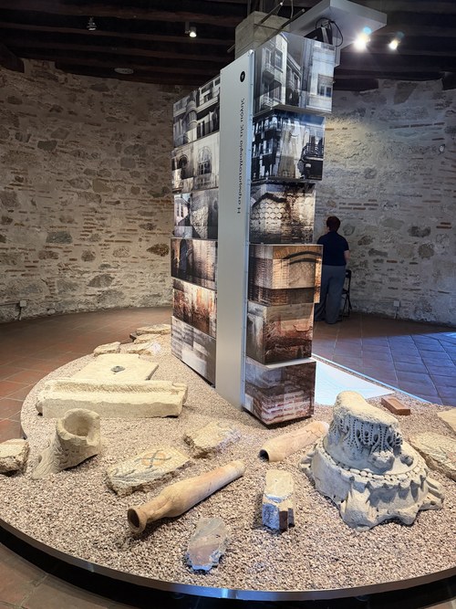 Stone artifacts and fragments displayed around a photo panel in a round brick room, White Tower of Thessaloniki and Museum, Greece
