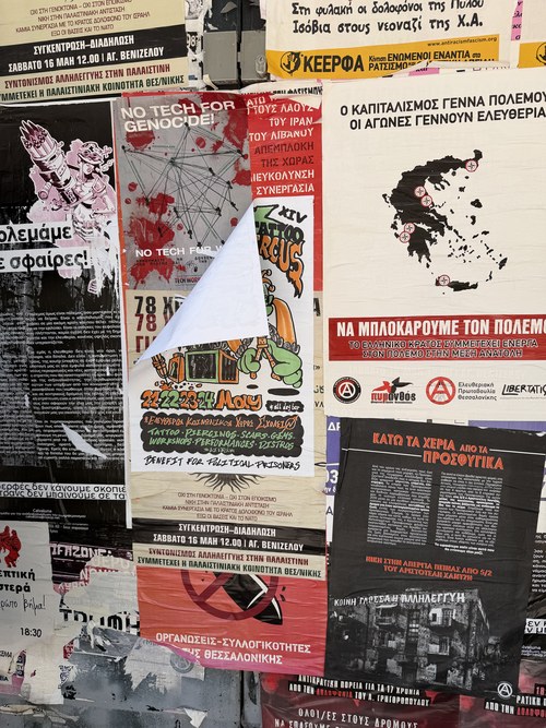 Wall covered in layered political posters in Greek and English, one corner peeling away, Palace of Galerius, Greece