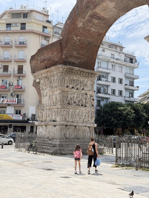 Carved stone pier and brick arch with two pedestrians walking past, Arch of Galerius, Greece