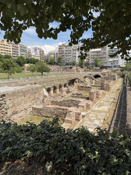 Sunken Roman ruins with brick walls and a stone-paved path under tree branches, Holy Church of St. Demetrius, Greece