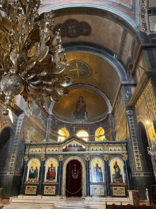 Gilded chandelier hanging before an ornate iconostasis and golden apse mosaic inside Hagia Sophia of Thessaloniki, Greece