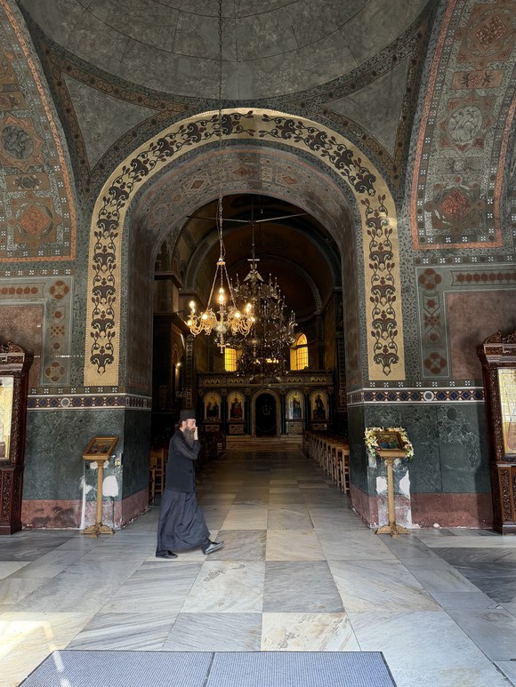 A man in a dark robe crosses the marble floor beneath a painted arch, Hagia Sophia of Thessaloniki, Greece