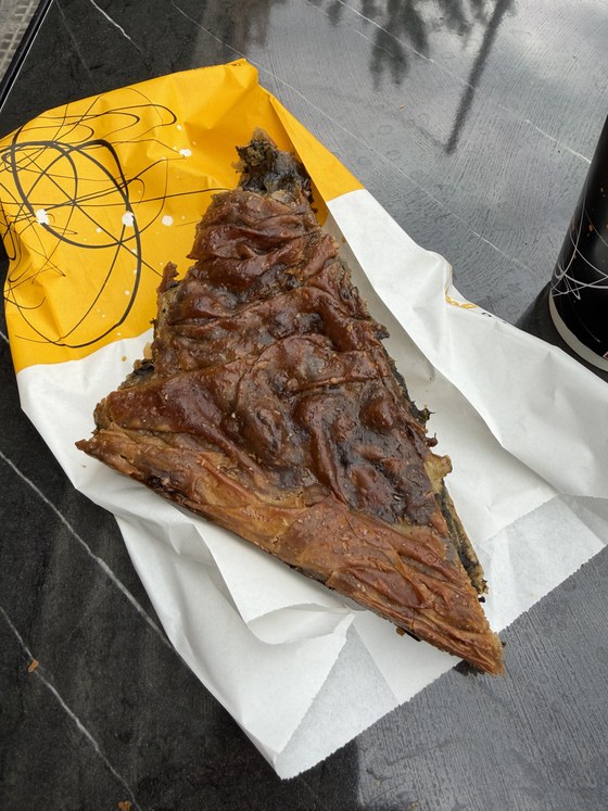Triangular slice of golden phyllo pie on a yellow and white paper wrapper, Hagia Sophia station, Greece