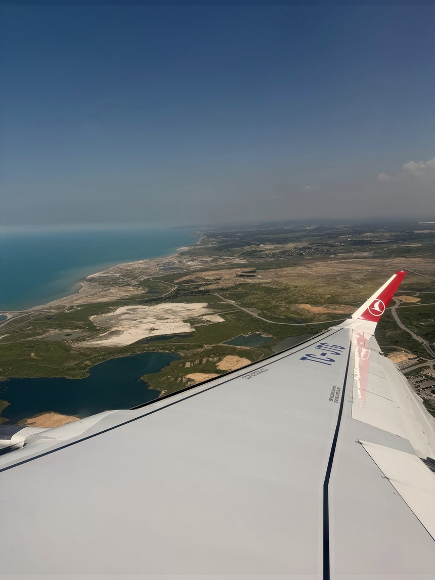 Airplane wing with a red Turkish Airlines winglet over a coastline, lakes and dry green land near Antalya, Turkiye