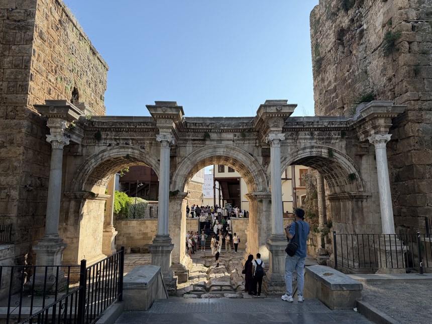 Triple-arched stone gateway with marble columns and crowds of visitors beyond, Antalya, Turkiye
