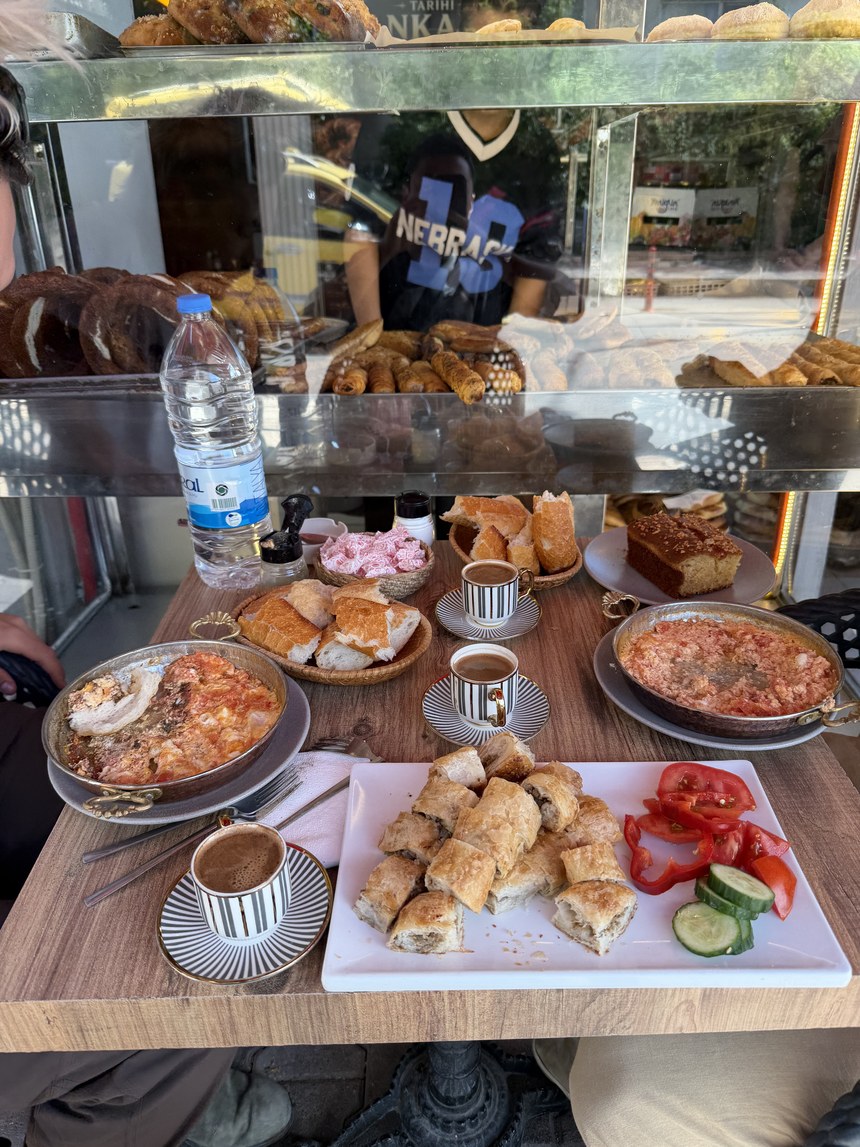 Table of pastries, egg dishes, vegetables and Turkish coffee beside a bakery display case, Antalya, Turkiye
