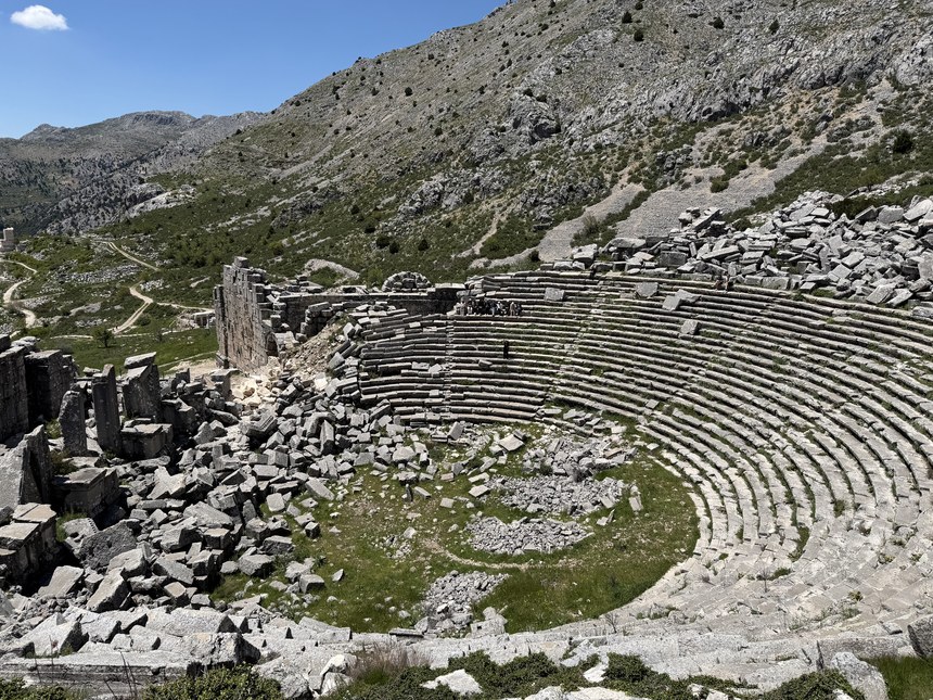 Curved stone seating of a ruined hillside theater with fallen blocks, Sagalassos, Türkiye