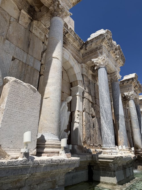 Marble columns, a statue in an arched niche and an inscribed stone beside a fountain pool, Sagalassos, Türkiye