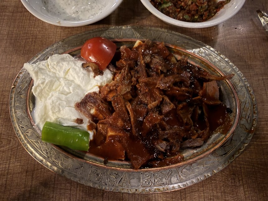 Sliced meat in tomato sauce with yogurt, a tomato and a green pepper on an engraved metal plate, Paşa Bey, Turkiye