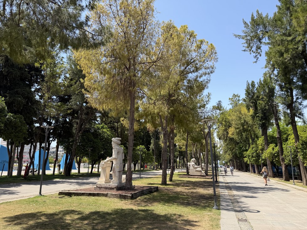 White stone statues among tall pine trees beside a shaded walking path, Karaalioğlu Park, Turkiye