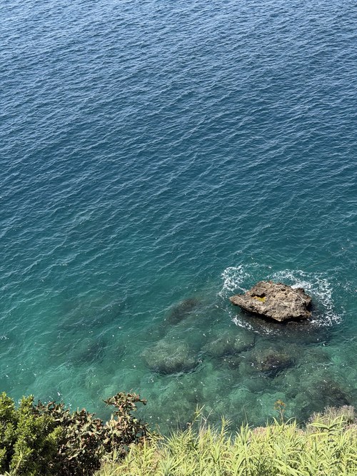 Rocky outcrop in clear turquoise water seen from a green clifftop, Antalya, Turkiye