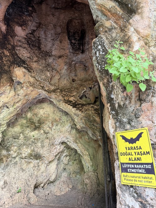 Rock cave entrance with a yellow bat habitat sign asking visitors not to enter, Upper Düden Falls, Turkiye