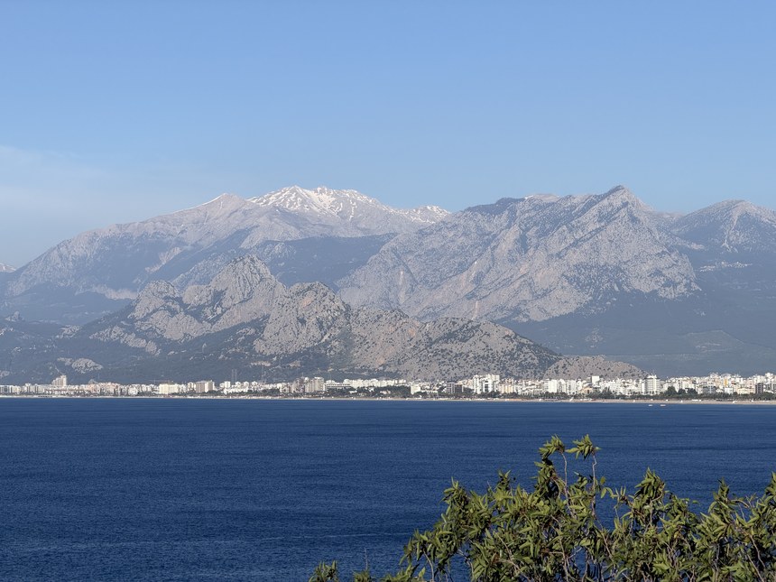 Snow-capped mountains rising behind a city along the deep blue sea, Antalya, Turkiye