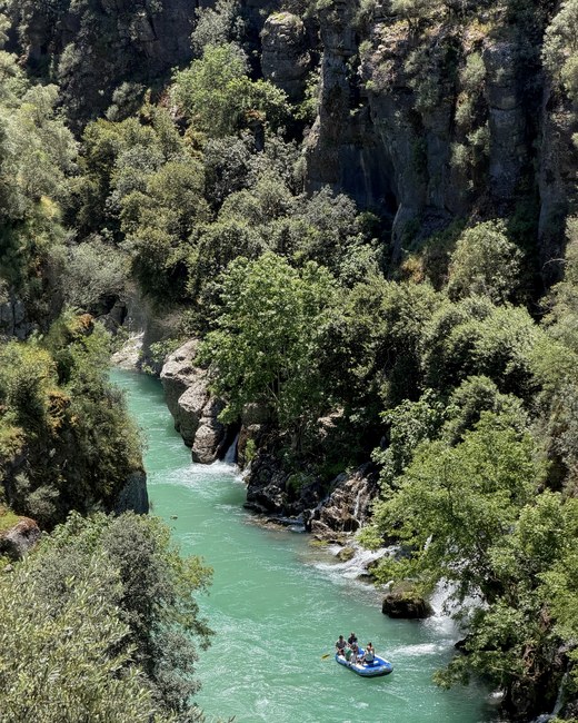 Blue raft of rafters floating down a turquoise river between steep green canyon walls, Köprülü Canyon, Turkiye