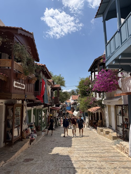 Cobbled shopping street with wooden balconies, pink bougainvillea and strolling visitors, Kaş, Turkiye