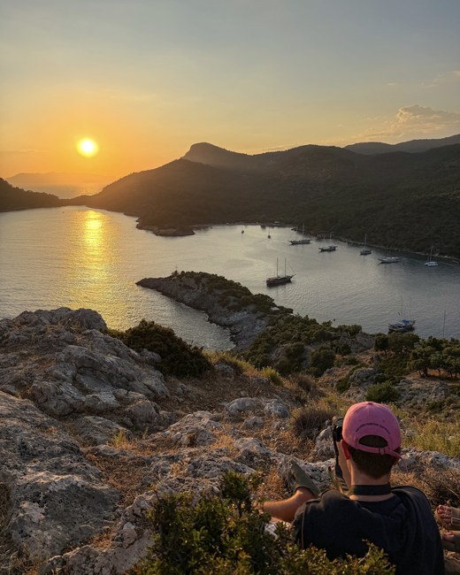 Traveler in a pink cap watching the sun set over a bay with anchored gulets, Santa Claus Island, Turkiye