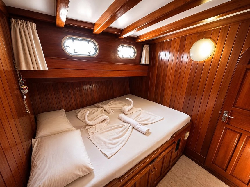 A wood-paneled double cabin on the Mr. Ceyhun with two portholes and towels folded on the bed