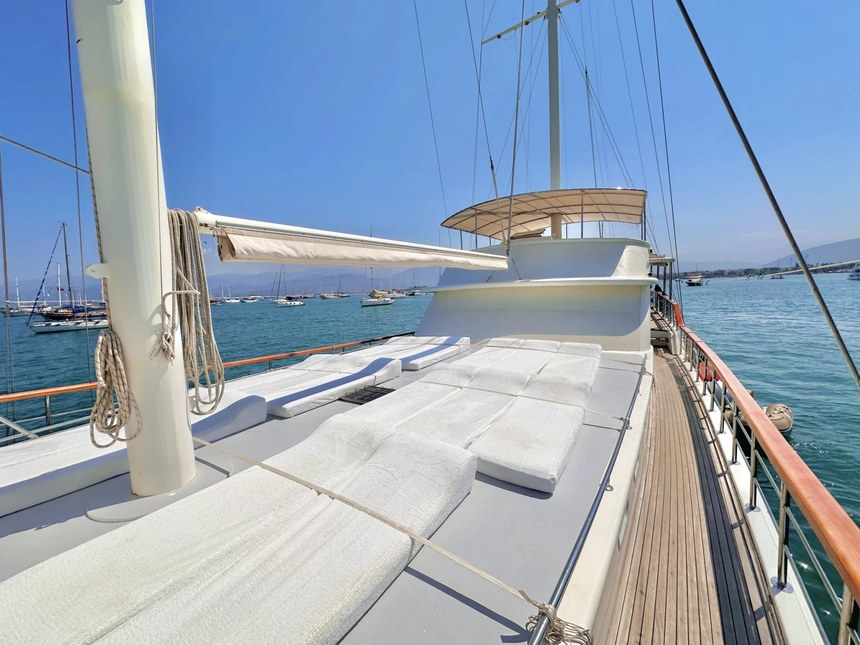 The front deck of the Mr. Ceyhun gulet, white sun cushions laid out under the mast with the harbor behind
