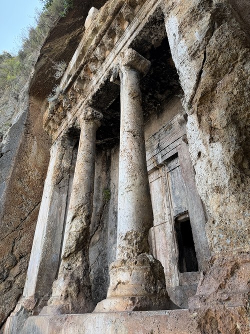 Low-angle view of a rock-cut tomb facade with weathered stone columns and a carved door, Ancient City of Telmessos, Turkiye