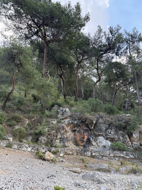 Painted portrait of a woman with long dark hair on a rock face below pine trees, Lycian Way near Fethiye, Turkiye
