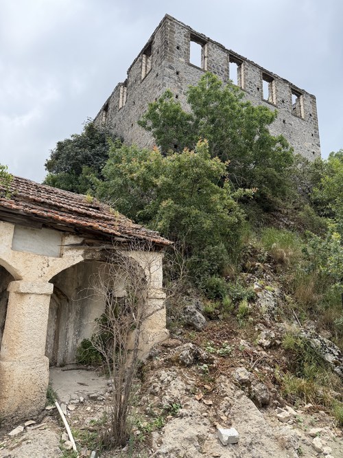 Roofless stone building with empty window frames above a tile-roofed arched porch on a rocky hillside, Kayaköy, Turkiye