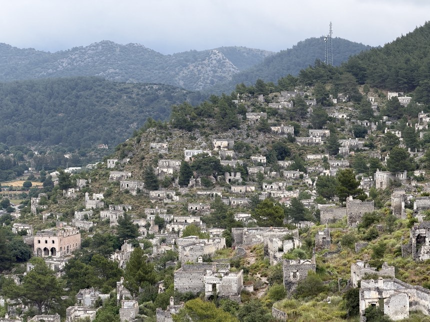 Rows of roofless stone houses on a pine-covered hillside beneath forested mountains, Kayaköy, Turkiye
