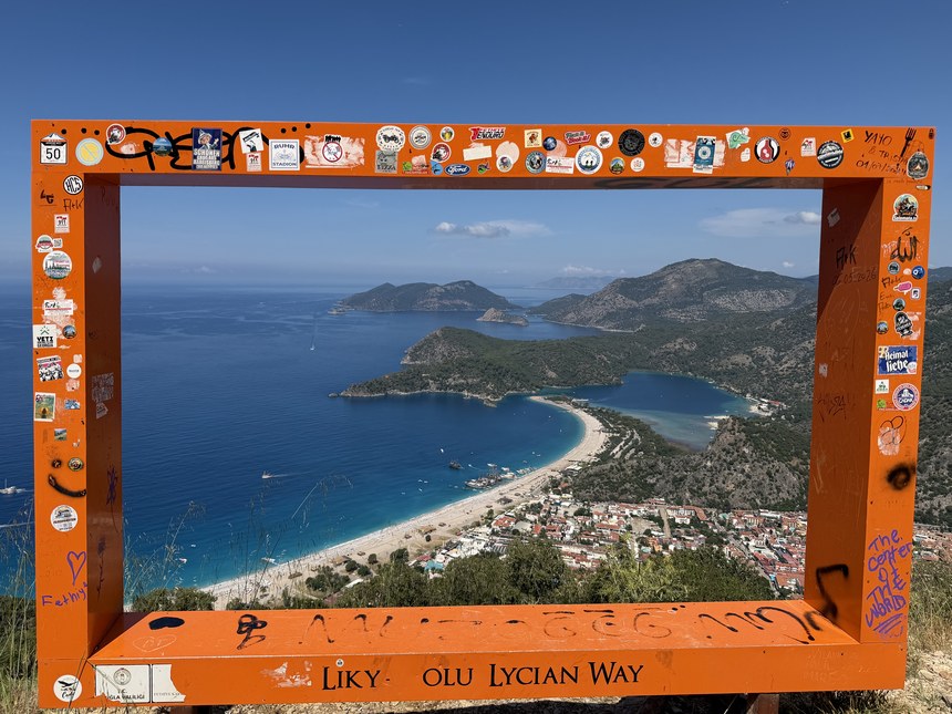 Orange sticker-covered Lycian Way photo frame overlooking the Blue Lagoon and the beach at Ölüdeniz, Turkiye