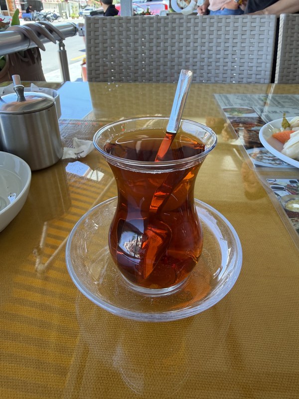 Tulip glass of black tea with a spoon on a saucer at a sunlit outdoor table, Blue Lagoon, Turkiye