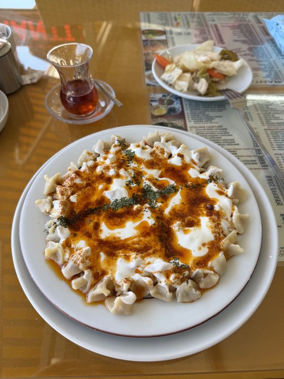 Plate of manti dumplings with yogurt, chili butter and dried mint beside a glass of tea, Blue Lagoon, Turkiye